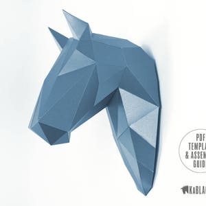 May include: A blue papercraft horse head model. The model is made of folded paper and has a geometric design. The model is a 3D representation of a horse's head.