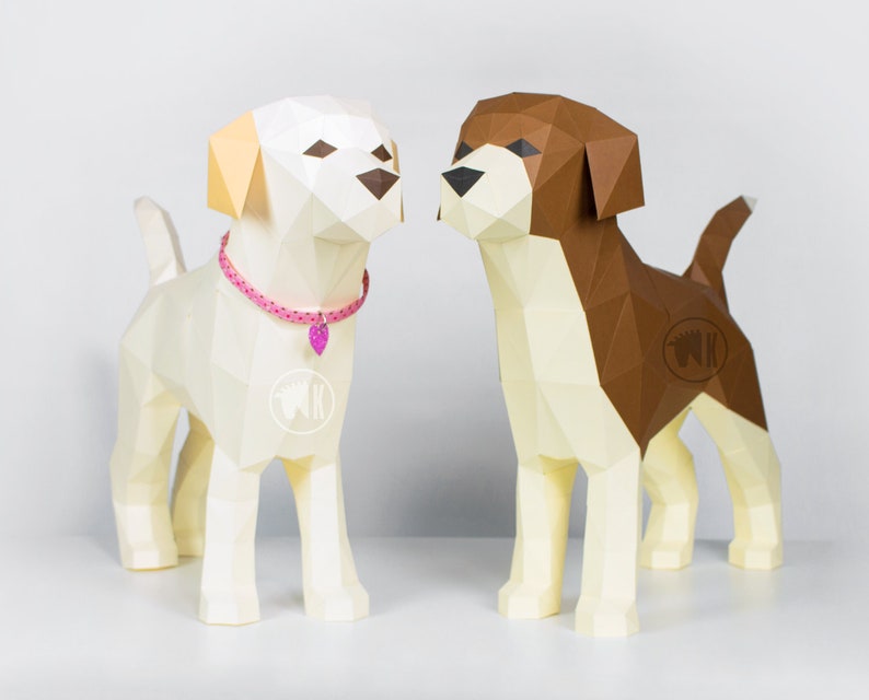 May include: Two papercraft dogs, one white with a pink collar and one brown and white, standing side by side on a white surface.