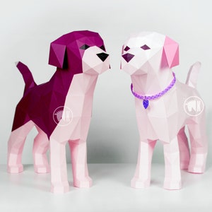 May include: Two papercraft dogs, one pink and one purple, are standing side-by-side. The pink dog is wearing a purple beaded collar with a heart charm.