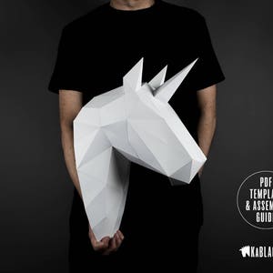 May include: A person holding a white papercraft unicorn head. The unicorn head is made of folded paper and has a 3D effect. The text "PDF TEMPLATE & ASSEMBLY GUIDE" is visible in the lower right corner of the image. The text "KABBLACKOUT" is visible in the lower right corner of the image.