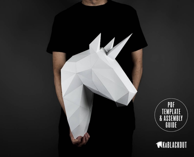 May include: A person holding a white papercraft unicorn head. The unicorn head is made of folded paper and has a 3D effect. The text "PDF TEMPLATE & ASSEMBLY GUIDE" is visible in the lower right corner of the image. The text "KABBLACKOUT" is visible in the lower right corner of the image.