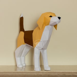 May include: A papercraft model of a beagle dog, standing on a white surface. The dog is made of white, brown, and yellow paper and has a triangular shape.