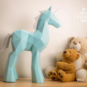 May include: A light blue papercraft unicorn model with a white mane and tail. The unicorn is standing on a wooden surface next to two teddy bears.