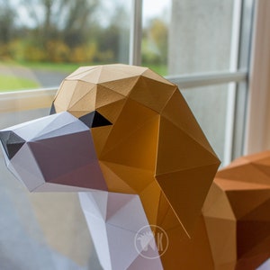May include: A papercraft model of a beagle dog, made from brown, white, and black paper. The dog is posed with its head turned to the side, looking towards the viewer. The model is partially assembled, with some of the paper pieces still attached.