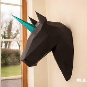 May include: Black papercraft unicorn head with a teal glitter horn mounted on a white wall.