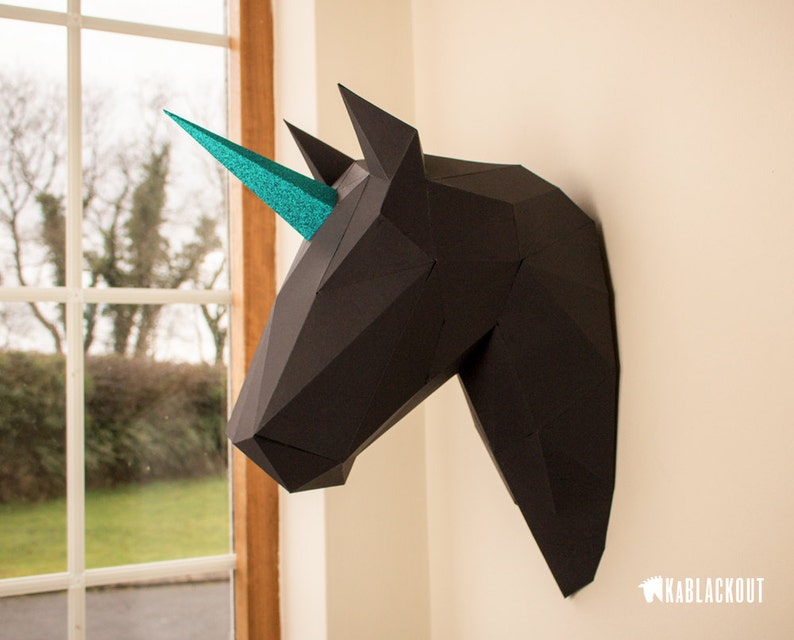 May include: Black papercraft unicorn head with a teal glitter horn mounted on a white wall.