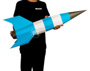 May include: A person holding a large blue and white paper rocket. The rocket has a gray nose cone and white stripes.