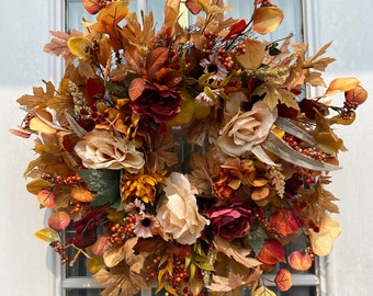 May include: A fall-themed wreath with a variety of faux flowers and leaves in shades of brown, orange, and red. The wreath is made of a natural material and features a variety of textures, including velvet, burlap, and silk.