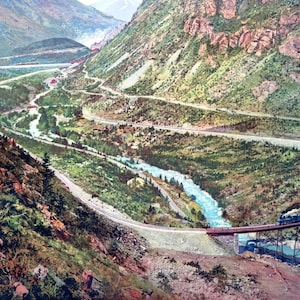 May include: A black train travels on a winding track through a mountainous landscape. The train is on a bridge over a river, and the track continues along the side of a steep cliff. The landscape is green and lush, with trees and rocks.