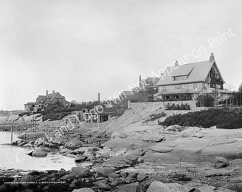 May include: A black and white photograph of two houses on a rocky coastline. The houses are both large and have multiple stories. The house in the foreground is closer to the camera and has a more modern design. The house in the background is further away and has a more traditional design. The houses are both surrounded by trees and bushes. The coastline is rocky and there is a body of water in the background.