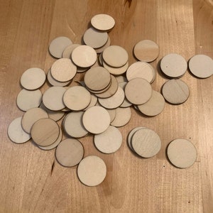 May include: A pile of round, unfinished wooden discs, scattered on a light brown wooden surface.