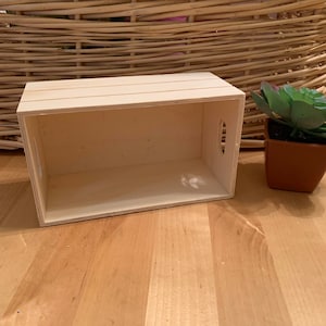 May include: A small, wooden box with a natural finish. The box has a rectangular shape and is empty. It is sitting on a wooden surface.