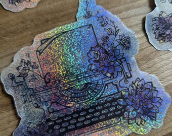 May include: A holographic sticker featuring a vintage typewriter with floral accents. The typewriter is outlined in black and has a rainbow iridescent finish. The sticker has the text "redbubble" in the bottom right corner.