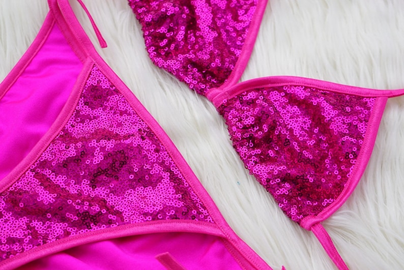 May include: A pink sequined bikini top with adjustable straps. The top is made of a soft, stretchy fabric and features a triangle shape.