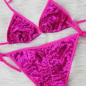May include: A pink sequined bikini top and bottom with thin pink straps. The bikini is made of a shiny, sparkly fabric.