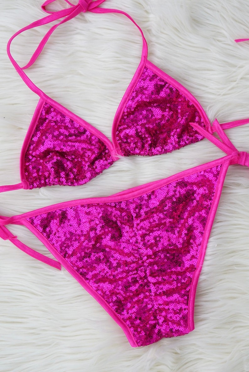 May include: A pink sequined bikini top and bottom with thin pink straps. The bikini is made of a shiny, sparkly fabric.