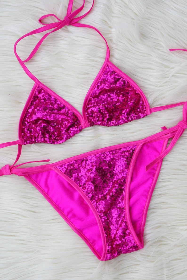 May include: A pink sequined bikini top and bottom. The bikini is made of a shiny fabric with a triangle top and a high-cut bottom.