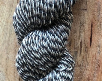 May include: A skein of black and white yarn with a speckled pattern. The yarn is made of wool and is soft and fluffy.