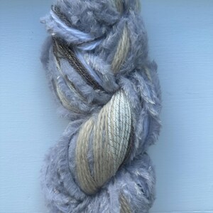 May include: A skein of yarn with a fluffy, gray texture, interwoven with beige and silver threads.