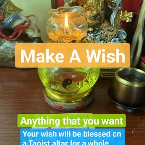 Puede incluir: Una lámpara de aceite de vidrio encendida con una llama, con el texto "Make A Wish" y texto adicional sobre bendiciones en un altar taoísta. La lámpara tiene un líquido amarillo y un símbolo del Yin Yang.