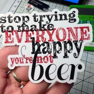 May include: A white sticker with black and red text that reads "stop trying to make everyone happy you're not beer". The sticker has a distressed, vintage look.