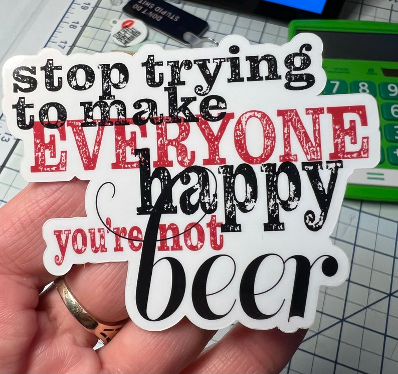 May include: A white sticker with black and red text that reads "stop trying to make everyone happy you're not beer". The sticker has a distressed, vintage look.