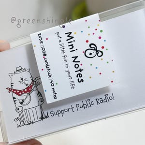 May include: A pack of 40 mini notes with a cute cartoon cat playing a banjo. The pack is labeled "Mini Notes" and "Support Public Radio!" The notes are 2x3.5 inches and are made of 100# cardstock.