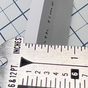 May include: A close-up of a metal ruler with markings in inches. The ruler is marked with numbers from 1 to 7. The text "6 & 12 PT. INCHES" is printed on the ruler.