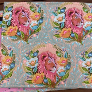 May include: A pink fabric with a repeating pattern of pink lions with brown manes, surrounded by colourful flowers and leaves on a light brown background.