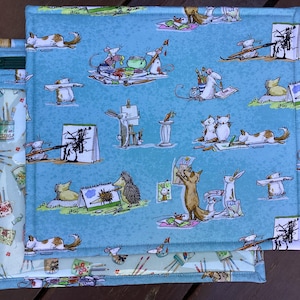 May include: A light blue fabric art supply case with a zip, featuring a whimsical pattern of cartoon animals creating art. The design includes mice, rabbits, foxes, and hedgehogs, with paintbrushes and art supplies. The case is rectangular.