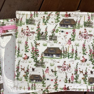 Op de afbeelding: Een witte stoffen etui met een rits en een roze rits. De stof heeft een herhalend patroon van huizen, bloemen, fietsen en kinderen.