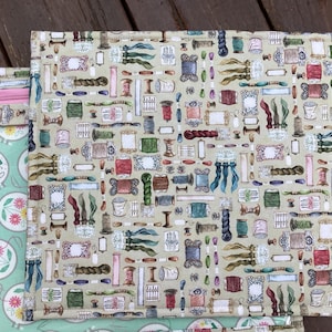 Op de afbeelding: Een groene en roze stoffen etui met een rits en een beige stoffen etui met een herhalend patroon van spoelen garen, naalden en andere naaigerei.
