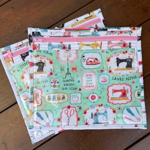 K&ouml;nnte beinhalten: Drei Rei&szlig;verschlusstaschen zum Thema N&auml;hen. Die Taschen haben einen hellgr&uuml;nen Hintergrund mit N&auml;hmaschinenillustrationen, floralen Akzenten und dem Text "A Stitch in Time Saves Nine". Die Rei&szlig;verschl&uuml;sse sind rosa.
