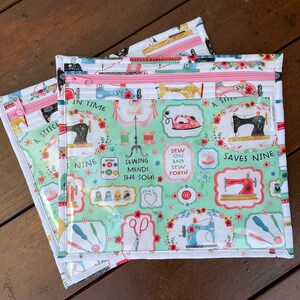 K&ouml;nnte beinhalten: Drei Rei&szlig;verschlusstaschen zum Thema N&auml;hen. Die Taschen haben einen hellgr&uuml;nen Hintergrund mit N&auml;hmaschinenillustrationen, floralen Akzenten und dem Text "A Stitch in Time Saves Nine". Die Rei&szlig;verschl&uuml;sse sind rosa.