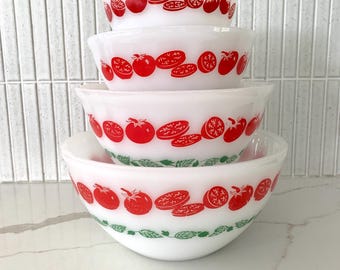 May include: A set of four white milk glass mixing bowls stacked vertically. Each bowl features a repeating pattern of bright red tomatoes and sliced tomatoes around the exterior. The two larger bowls also include a green leafy vine border design.