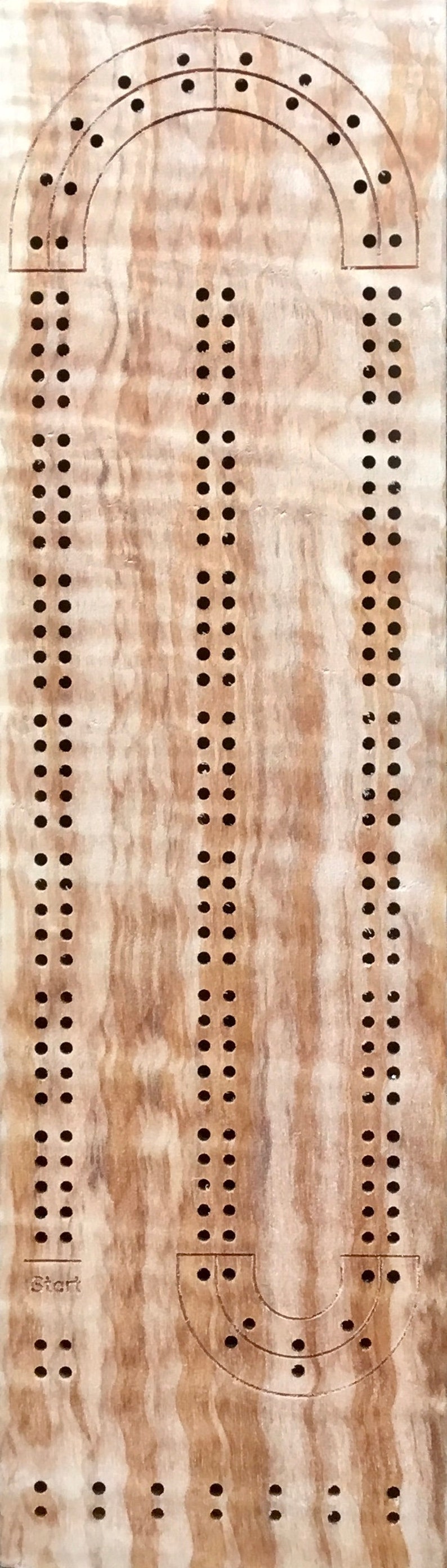 May include: A wooden cribbage board with a light brown stain. The board has two sets of holes for pegs, a start area, and two scoring areas. The board is made of wood with a natural grain pattern.