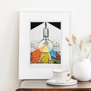 May include: A framed print of a lightbulb with a colourful geometric design radiating from it. The design includes a variety of shapes, colours, and patterns, including triangles, circles, and zigzags. The lightbulb is suspended from a cord and has a black background.