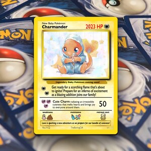 May include: A yellow and white Pokemon trading card featuring a cartoon illustration of a baby Charmander wearing a blue onesie. The card has the text "New Baby Pokemon Charmander" and "2023 HP" at the top. The card also has text describing the Pokemon's abilities and stats.