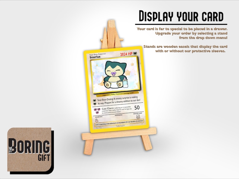May include: A yellow and white Pokemon card featuring a cartoon Snorlax with a baby pacifier. The card is displayed on a wooden easel stand. The text on the card reads "Snorlax 2024 HP".