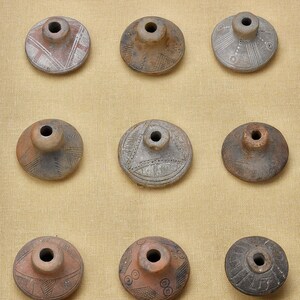 Puede incluir: Nueve piezas de cer&aacute;mica con diferentes dise&ntilde;os y patrones. Las piezas se muestran en un marco de madera sobre un fondo de tela beige.