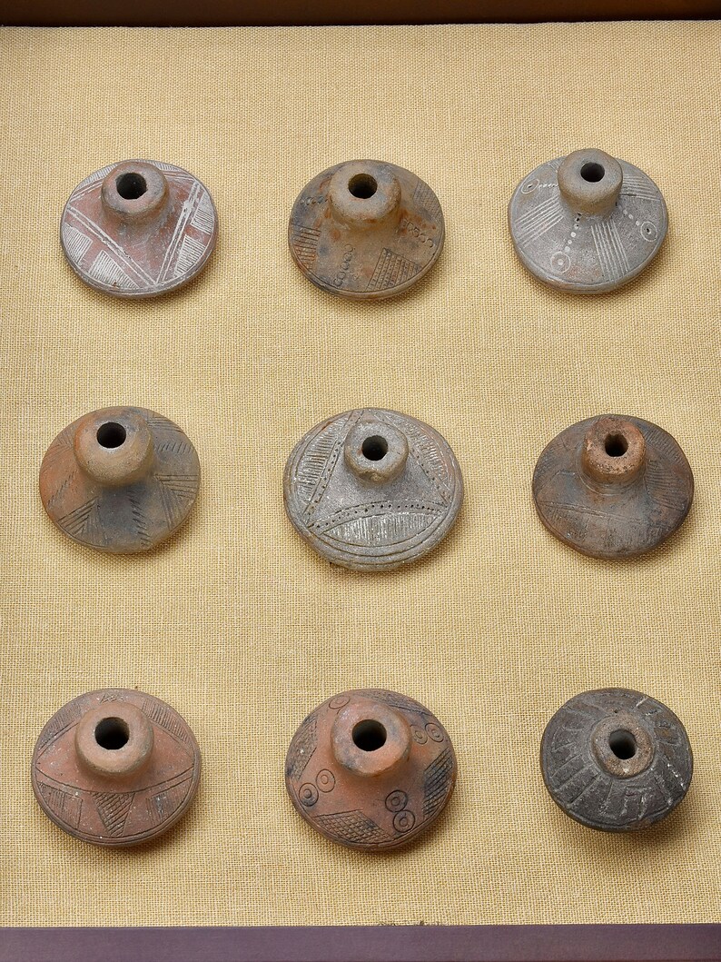 Puede incluir: Nueve piezas de cer&aacute;mica con diferentes dise&ntilde;os y patrones. Las piezas se muestran en un marco de madera sobre un fondo de tela beige.