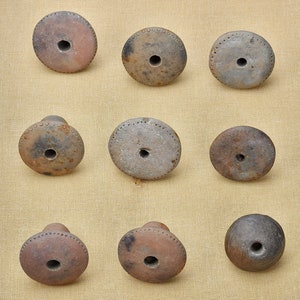 Puede incluir: Nueve piezas redondas de cer&aacute;mica de arcilla marr&oacute;n con un agujero en el centro. Las piezas est&aacute;n dispuestas en tres filas de tres.