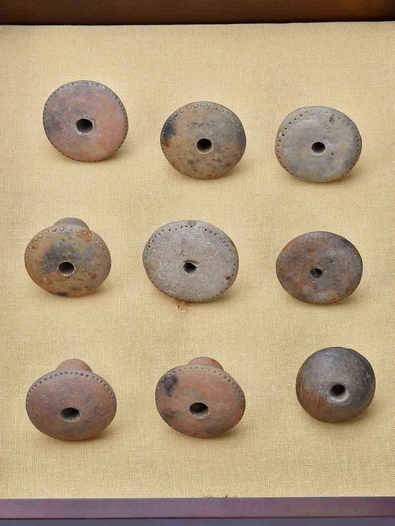 Puede incluir: Nueve piezas redondas de cer&aacute;mica de arcilla marr&oacute;n con un agujero en el centro. Las piezas est&aacute;n dispuestas en tres filas de tres.
