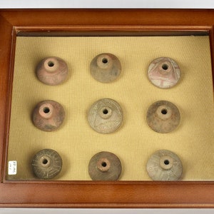 Puede incluir: Nueve peque&ntilde;os recipientes redondos de cer&aacute;mica de terracota con dise&ntilde;os intrincados se muestran en un marco de madera con un paspart&uacute; beige. Los recipientes tienen un peque&ntilde;o agujero en el centro de la parte superior.