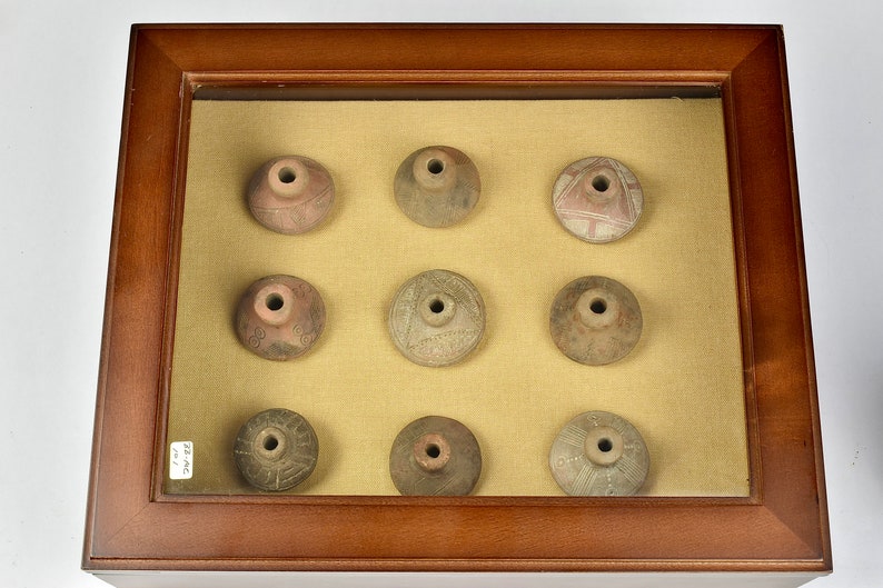 Puede incluir: Nueve peque&ntilde;os recipientes redondos de cer&aacute;mica de terracota con dise&ntilde;os intrincados se muestran en un marco de madera con un paspart&uacute; beige. Los recipientes tienen un peque&ntilde;o agujero en el centro de la parte superior.