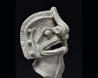 Puede incluir: Una escultura de cerámica blanca de un rostro estilizado con una gran boca abierta y detalles elaborados. La escultura está de perfil y tiene una superficie texturizada.