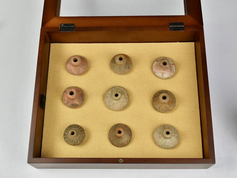 Puede incluir: Una caja de madera con tapa de vidrio muestra nueve peque&ntilde;os objetos redondos de cer&aacute;mica. Los objetos est&aacute;n decorados con varios patrones y dise&ntilde;os en tonos marrones, blancos y rojos.