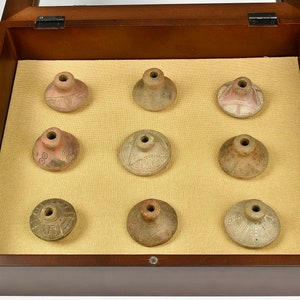 Puede incluir: Nueve peque&ntilde;os recipientes de cer&aacute;mica de terracota redondos con dise&ntilde;os intrincados se muestran en una caja de madera con tapa de vidrio.