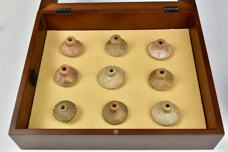 Puede incluir: Nueve peque&ntilde;os recipientes de cer&aacute;mica de terracota redondos con dise&ntilde;os intrincados se muestran en una caja de madera con tapa de vidrio.