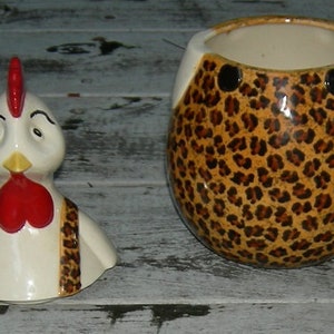 Puede incluir: Una jarra de galletas de cer&aacute;mica con forma de gallo con un dise&ntilde;o de estampado de leopardo. El gallo tiene una cresta y una papada rojas, plumas blancas y un babero de estampado de leopardo negro y marr&oacute;n.